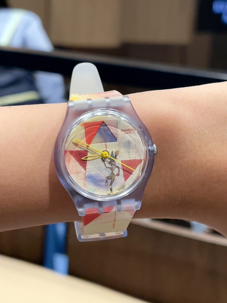 Swatch x Guggenheim 系列腕表，表盘与哑光透明表带饰有保罗·克利 (Paul Klee) 艺术作品《The Bavarian Don Giovanni》印花。